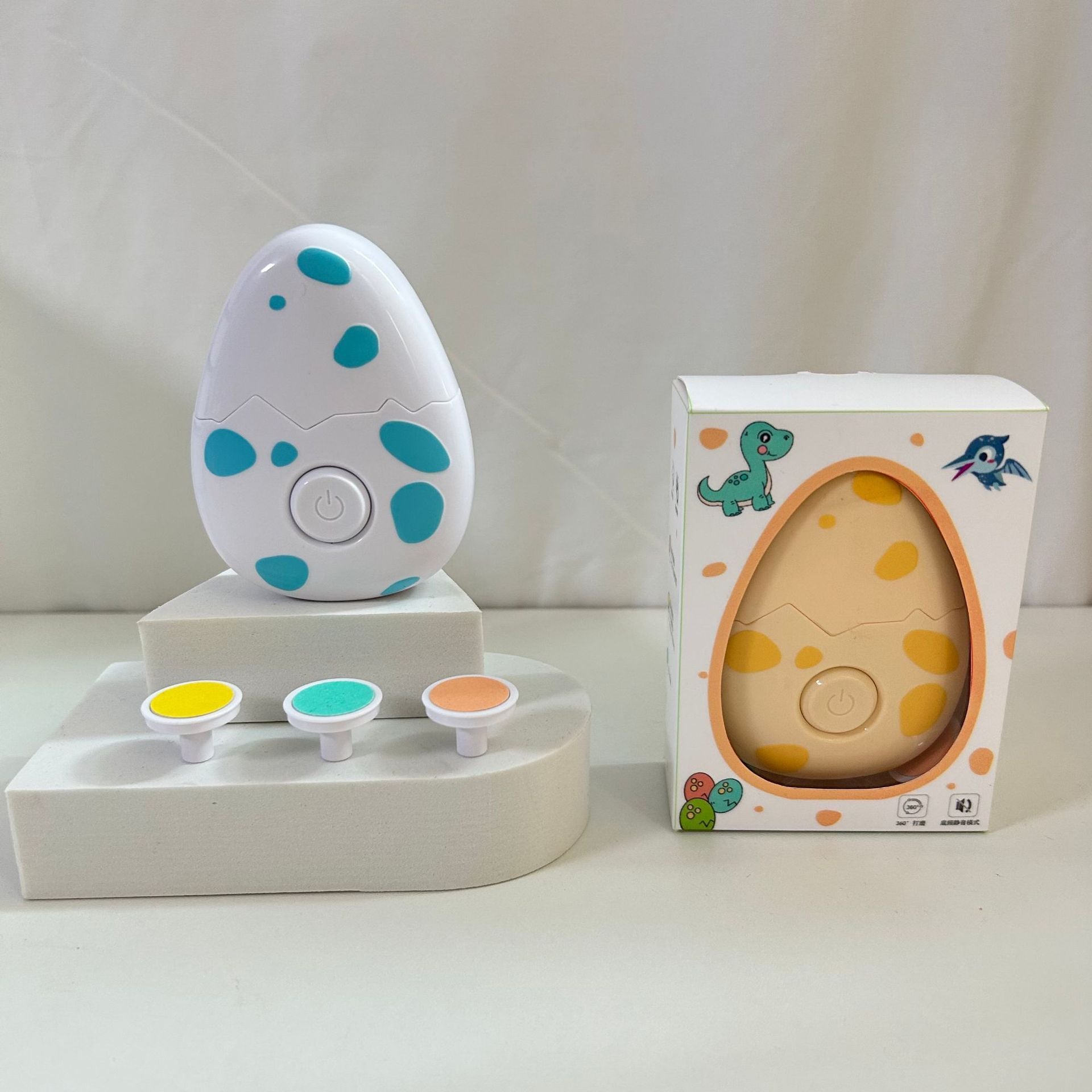 Egg-shaped Children electric nail grinder with soft grinding head for safe baby nail trimming with polka dot design and three color samples on a white surface, next to its packaging