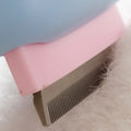Pink pet grooming brush with a comb on a white surface with pet hair