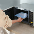 Person using a microwave oven with a blue plate inside; Reusable microwave-safe silicone storage bag in powder pink