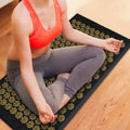 Person sitting on a acupressure mat on a wooden floor