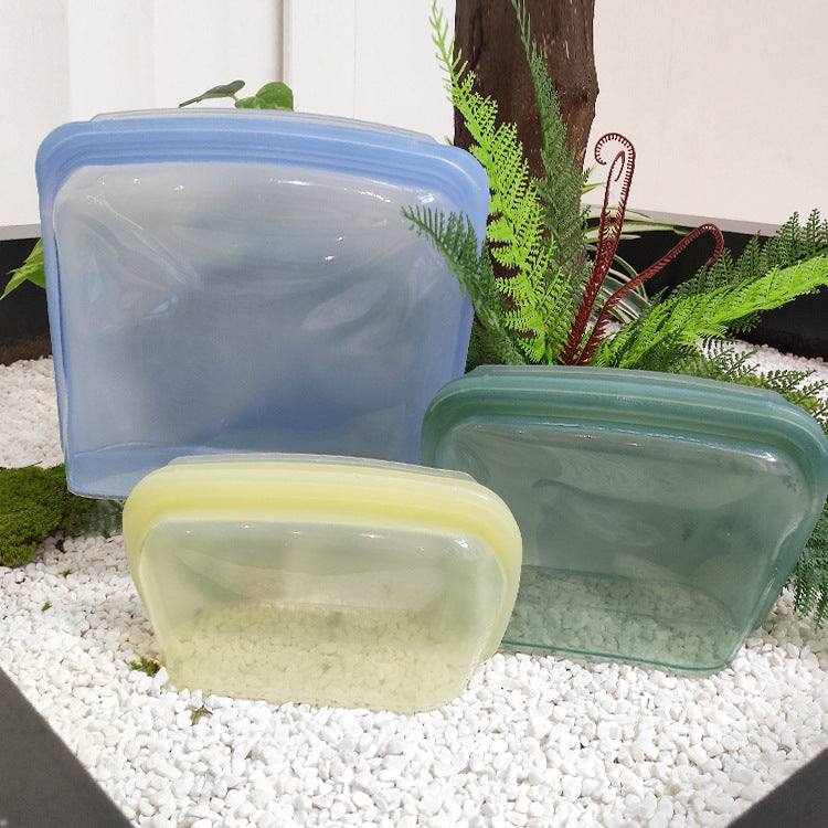 Set of colorful silicone food storage containers on a white surface with a blurred background; Oversized reusable silicone storage bags in assorted colors