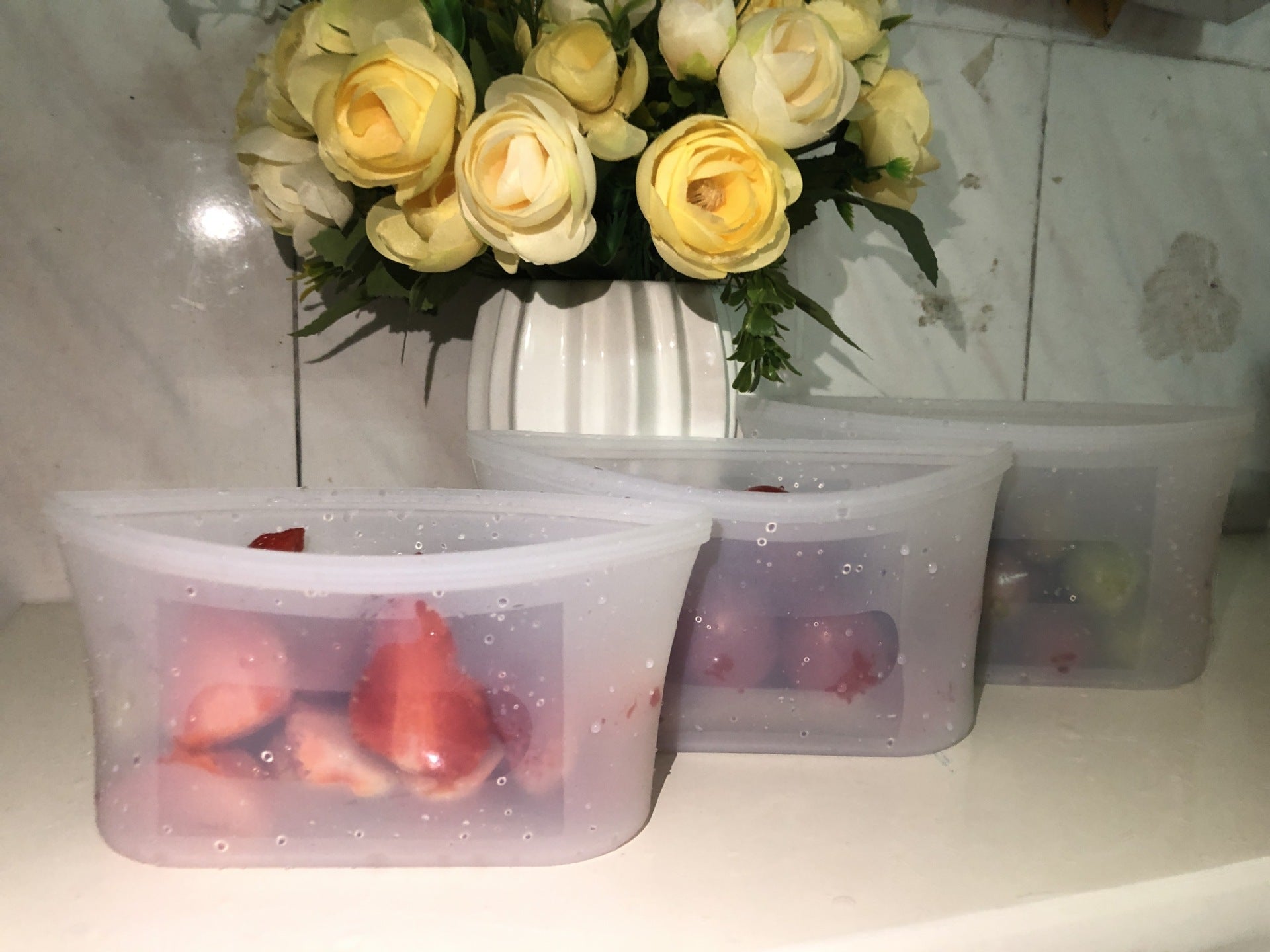 Two plastic containers with red and pink contents on a surface with a vase of yellow flowers in the background; Microwave & dishwasher safe silicone food containers