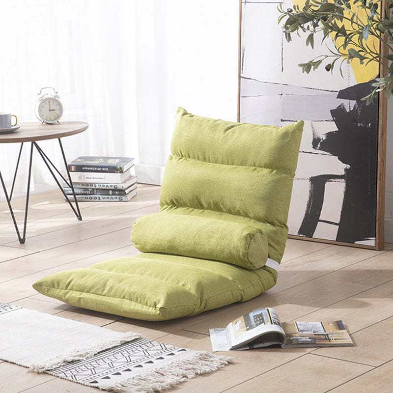 Green floor pillow on a wooden floor with a table and books in the background