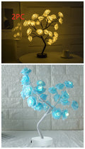 Two LED rose tree lights, one yellow and one blue, on a table with a white brick wall background
