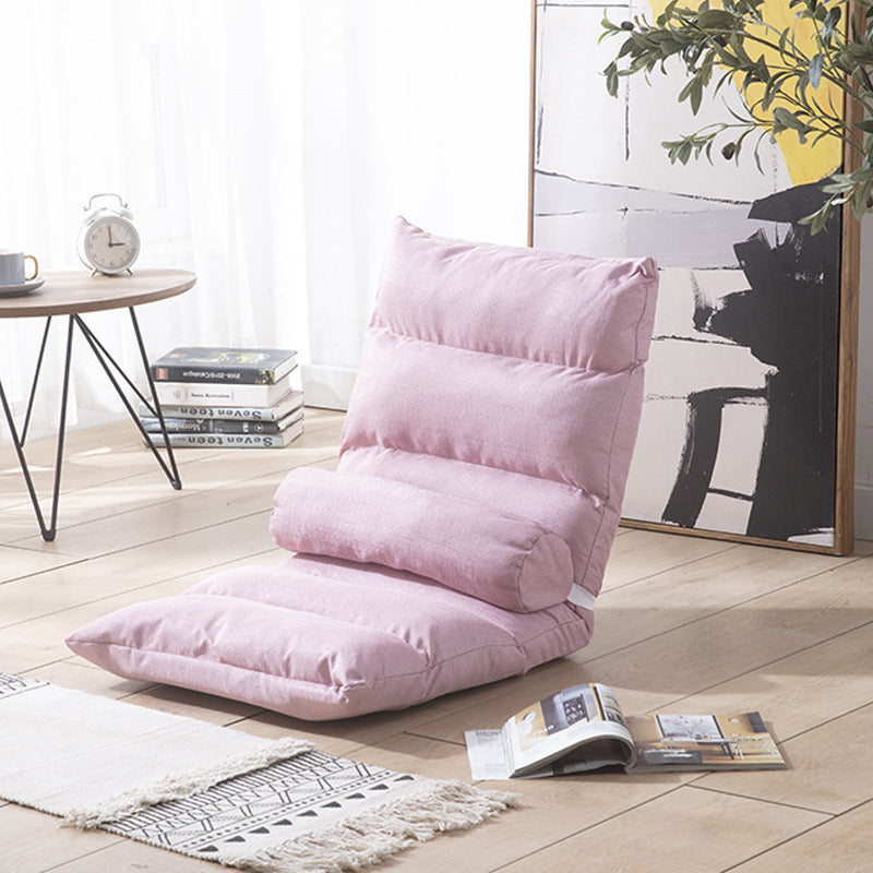 Pink floor pillow on a wooden floor with a table and books in the background
