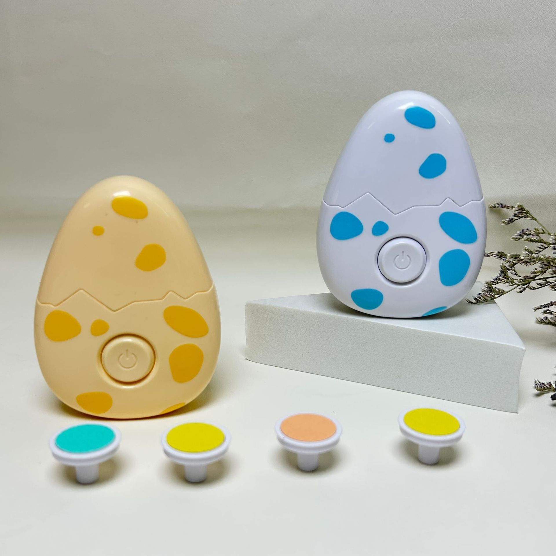 Two egg-shaped Children electric nail grinder with soft grinding head for safe baby nail trimming with colorful spots on a white background