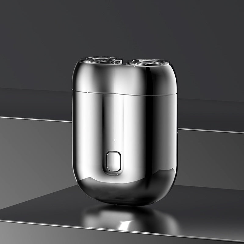 Silver electric shaver on a reflective surface with a dark background; Mini portable rechargeable electric shaver for men with floating cutter head and low-noise motor