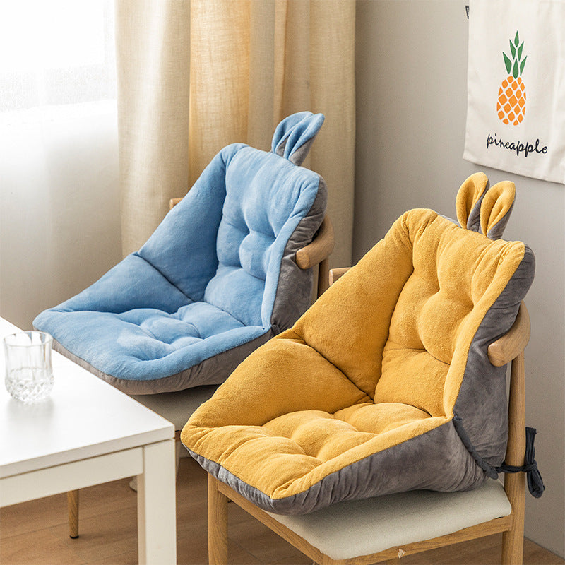 Two chair cushions with bunny ears, one blue and one yellow, on a wooden chair in a room; Plush backrest-integrated chair cushion in neutral color