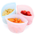 Three silicone snack bags filled with chips, carrots, and cherry tomatoes on a white background.