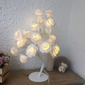 Decorative lamp with white rose lamp on a wooden surface against a textured white wall.