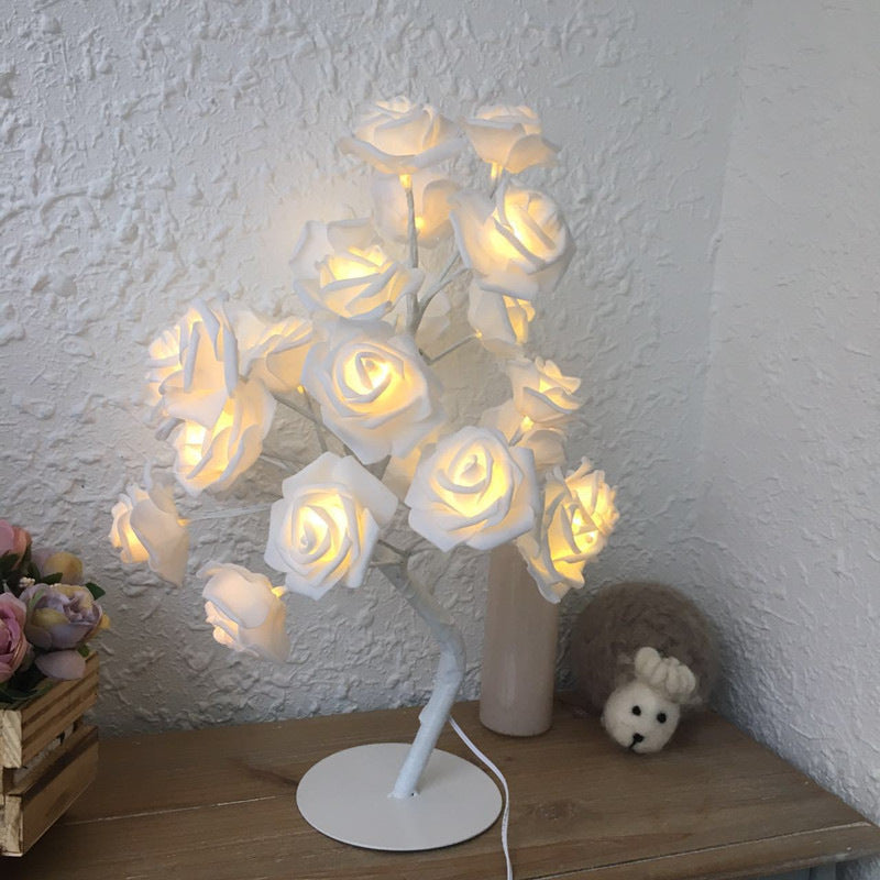 Decorative lamp with white rose lamp on a wooden surface against a textured white wall.