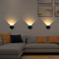 Modern living room with a gray sectional sofa, orange and black cushions, and wall-mounted lights