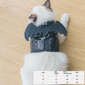 Cat wearing a sequined bat costume on a wooden floor with size chart overlay.