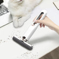 Hand using a small handheld vacuum cleaner on a desk with a cat in the background