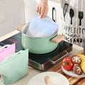 Person using a silicone lid on a pot with kitchen items and food in the background; Leakproof and BPA-free silicone storage bag for kitchen use