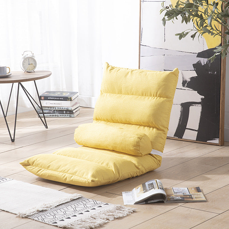 Yellow floor pillow in a room with a table, books, and a plant