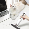 Cat sitting on a desk next to a laptop with a hand holding a cleaning tool.