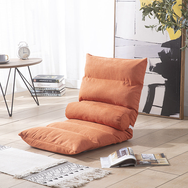 Orange floor pillow on a wooden floor with a table and books in the background