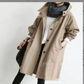 Person wearing a beige trench coat with a plain background
