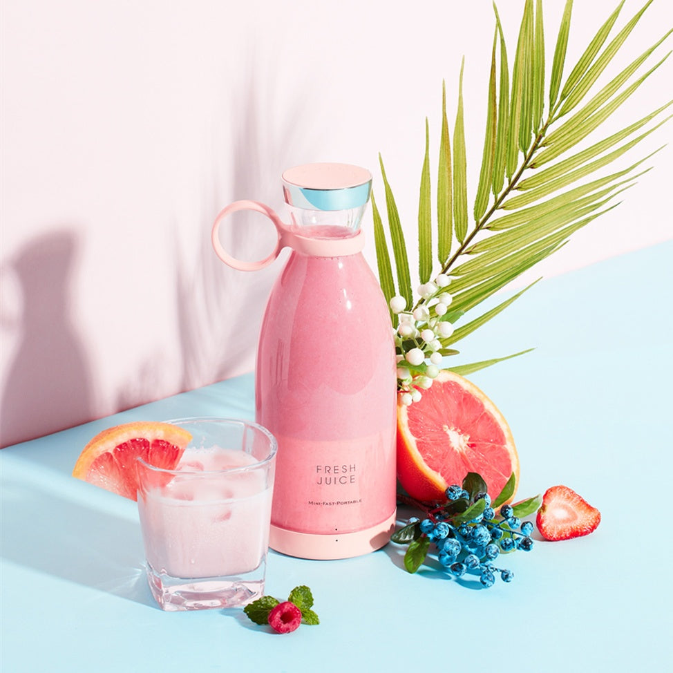 Pink Portable rechargeable USB blender with a glass of pink juice, grapefruit, and strawberry on a light blue background