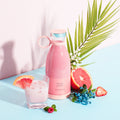 Pink Portable rechargeable USB blender with a glass of pink juice, grapefruit, and strawberry on a light blue background