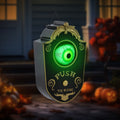 Halloween-themed doorbell cover with glowing green eye and 'Push to Ring' text, set against a blurred outdoor background.