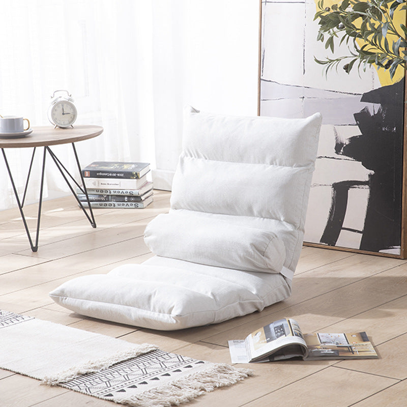 White floor pillow on a wooden floor with a table and books in the background