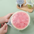 Person holding a watermelon slice covered with a silicone lid on a light green surface