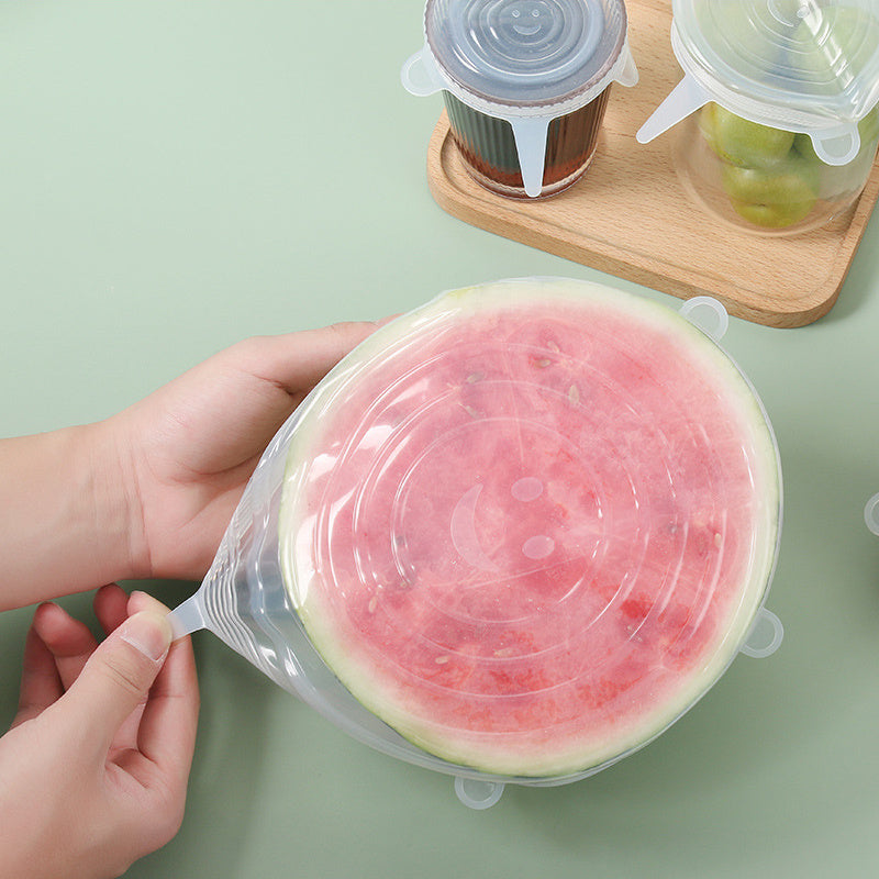 Person holding a watermelon slice covered with a silicone lid on a light green surface