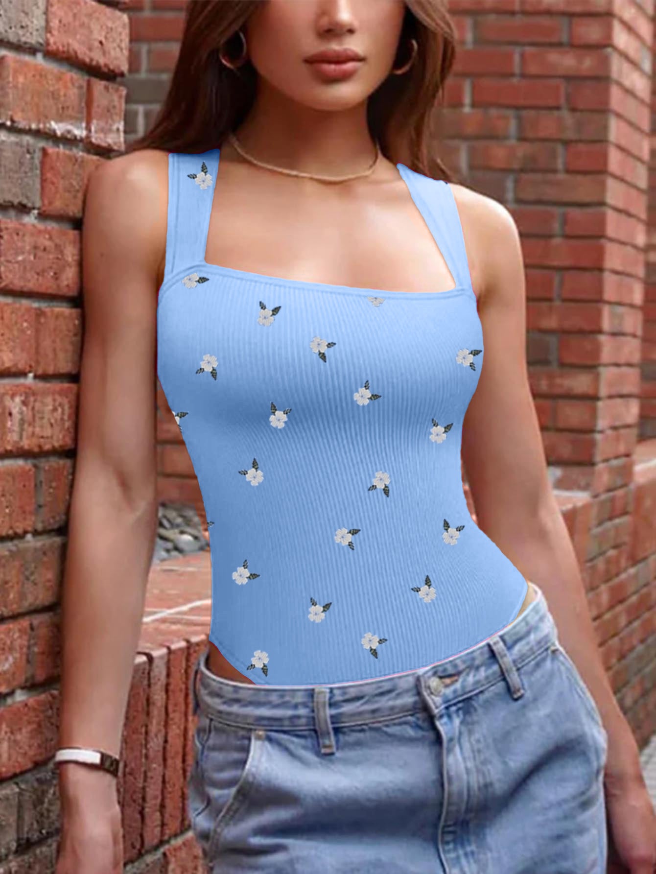 Person wearing a blue tank top with floral patterns against a brick wall.